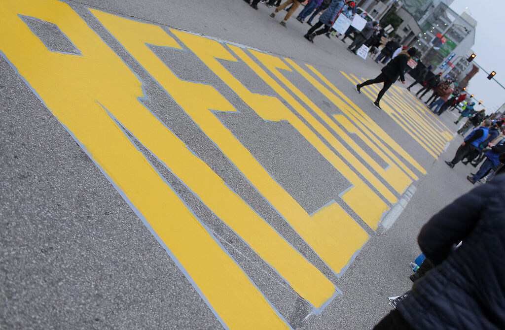 A protester walks between the words "Resign Hawley" painted on South Broadway